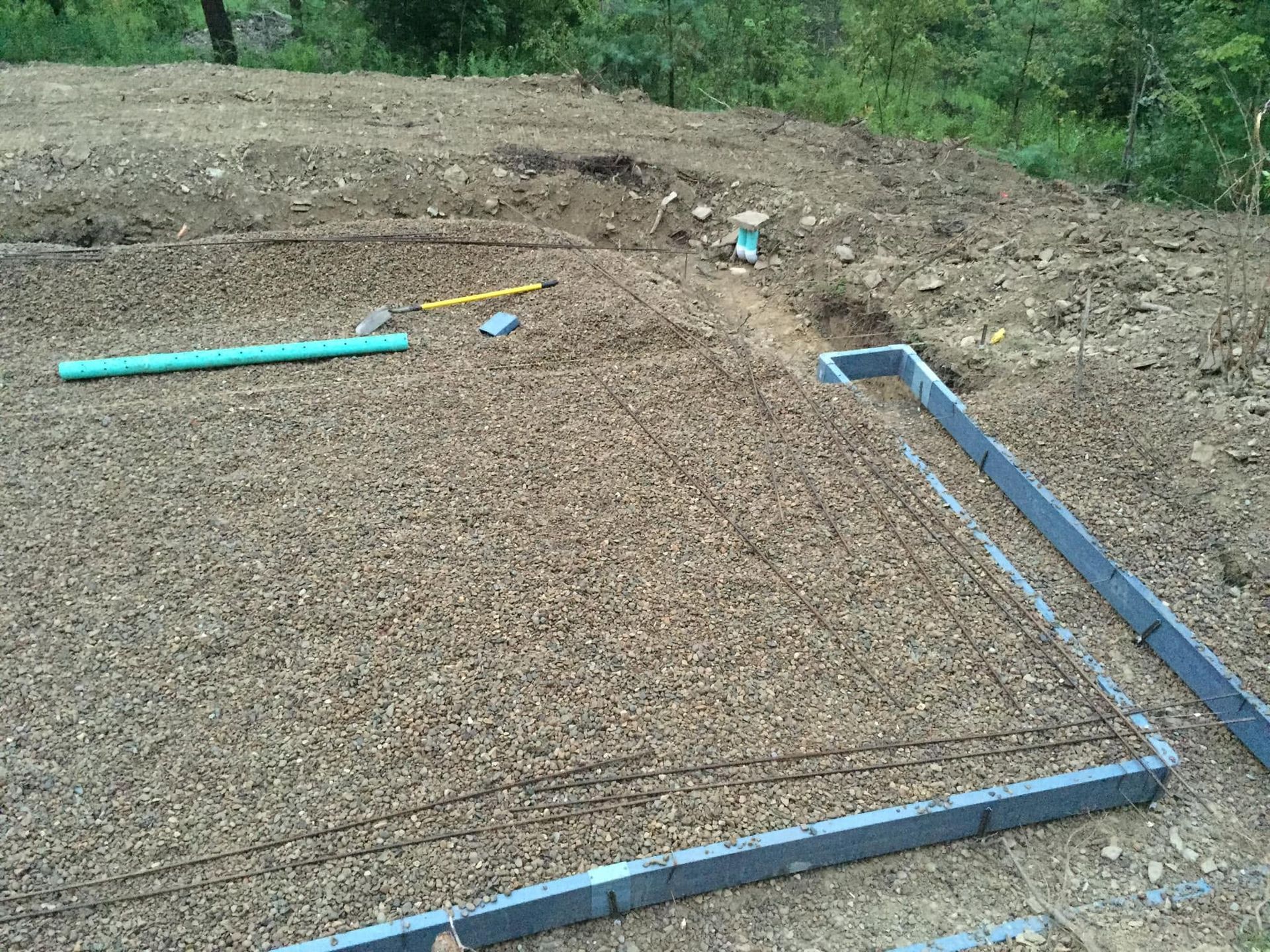 Blue PVC pipe outline on dirt lot, marking a rectangular foundation area in a wooded outdoor site