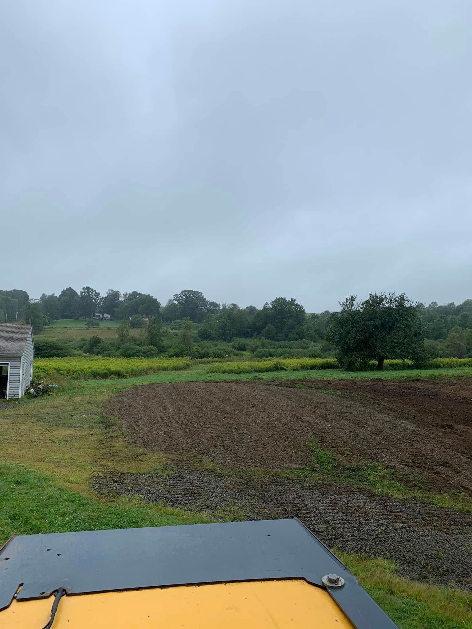 Rural field under a cloudy sky, seen from a tractor with a yellow hood in the foreground