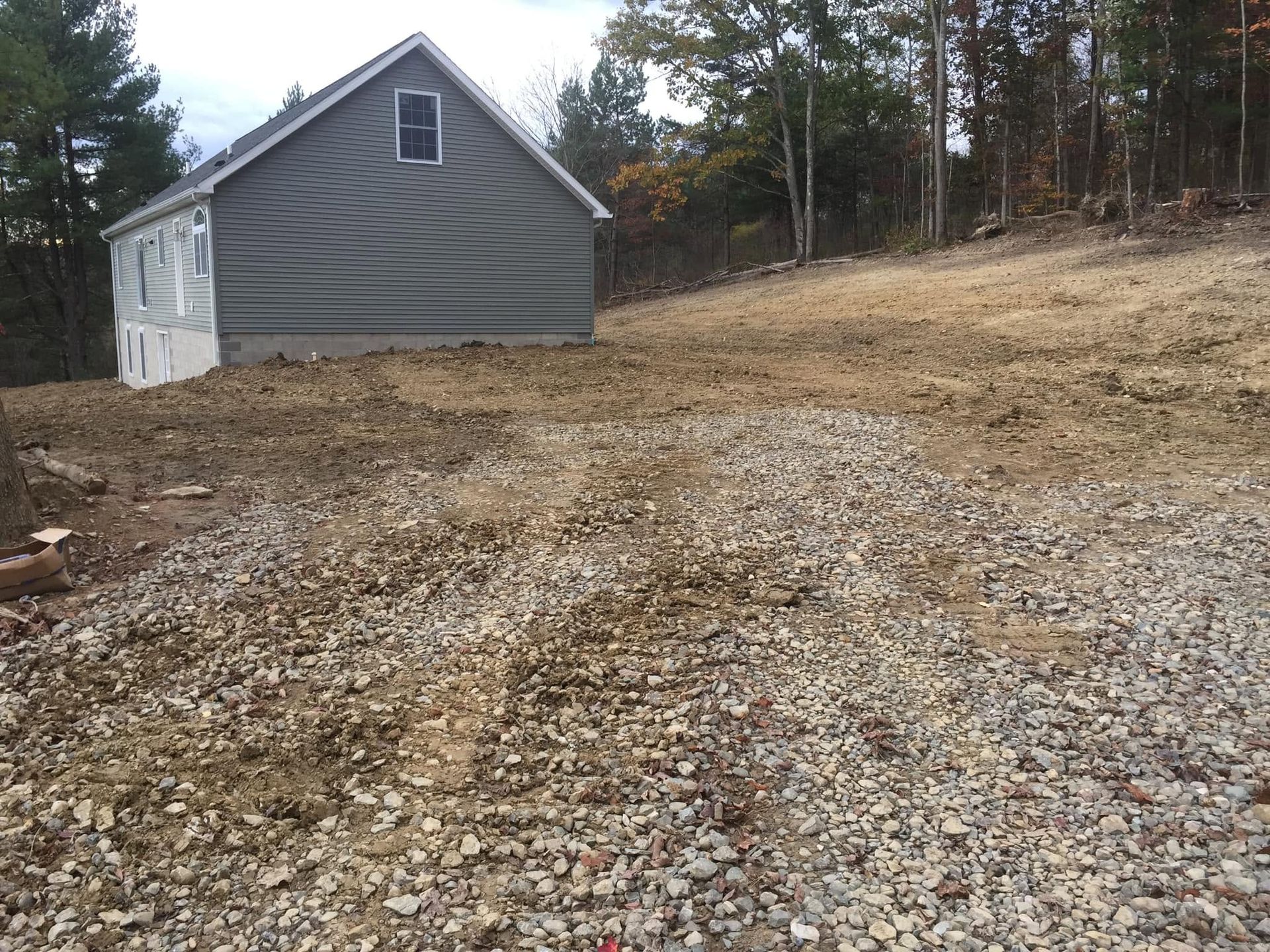 Gravel driveway beside a gray barn-like shed on a wooded rural lot