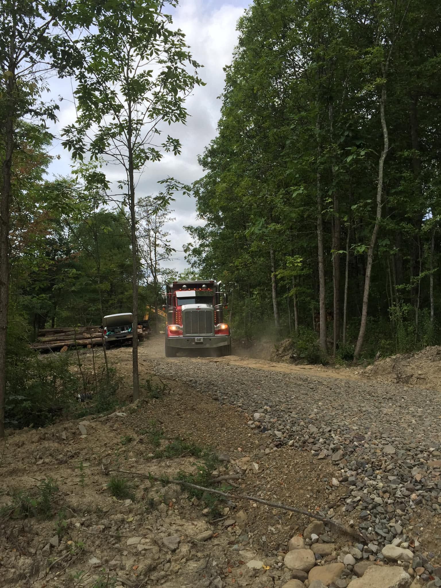 Red truck on a gravel road in a wooded forest clearing with cloudy sky.