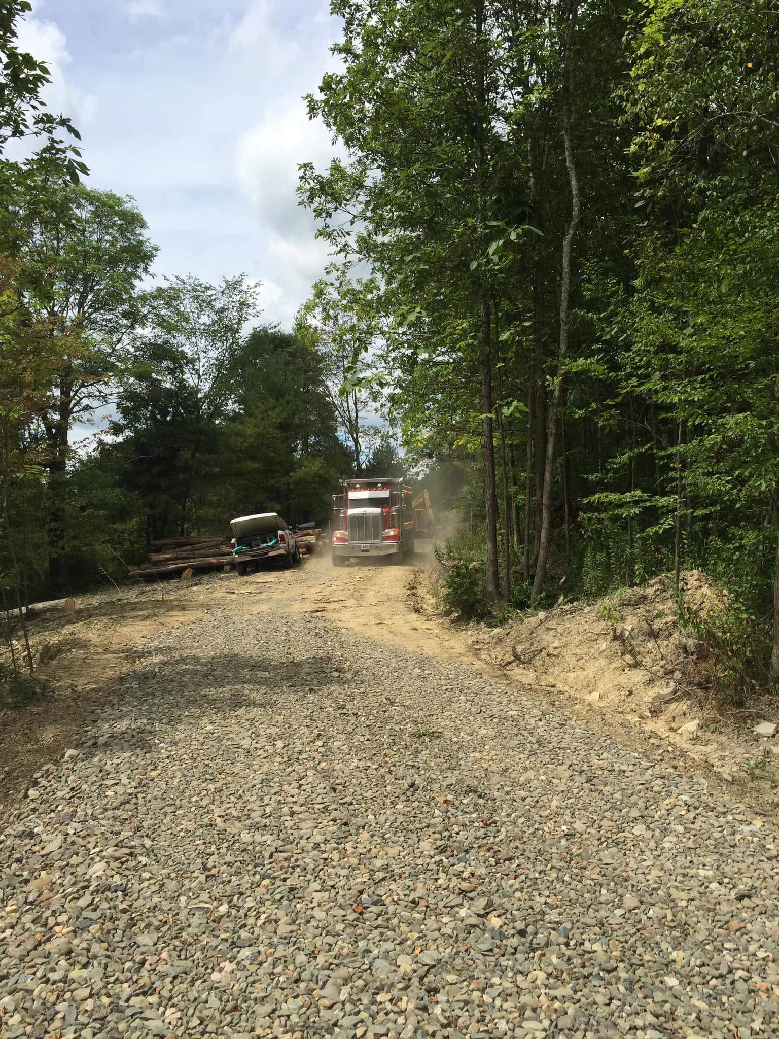 Gravel road through wooded area with a dump truck and equipment in the distance