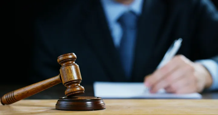 Wooden gavel in foreground, judge in suit writing in background.