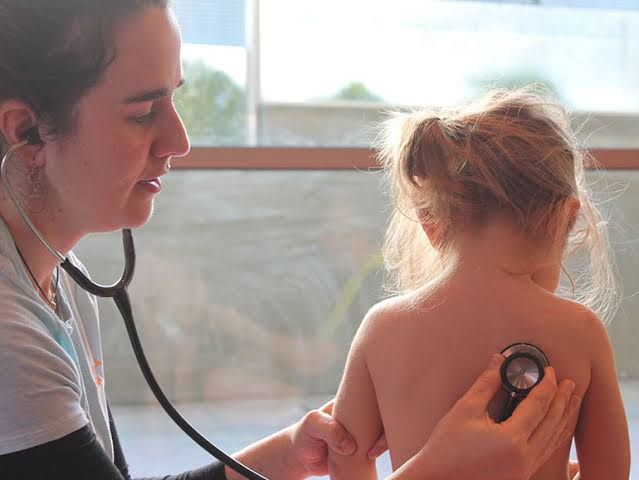 Un médico ausculta la espalda de un niño con un estetoscopio en una luminosa sala de consulta.