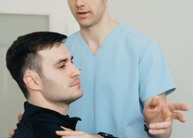 Fisioterapeuta ayudando a un hombre sentado con un estiramiento de cuello.