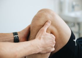 Manos presionando una rodilla doblada durante un masaje de piernas o una sesión de fisioterapia.