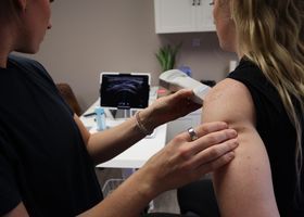 Médico realizando una ecografía en el brazo de un paciente en una sala de exploración médica.
