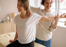 Dos personas estirándose en una habitación luminosa, sonriendo y vistiendo camisetas blancas.
