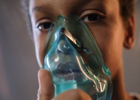 Niño con una máscara de oxígeno transparente, mirando a la cámara.