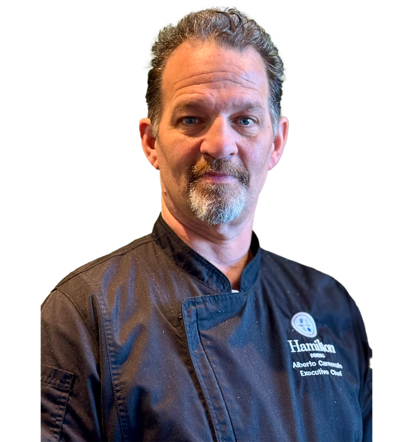 A chef in a black uniform with a Hamilton logo, looking forward.