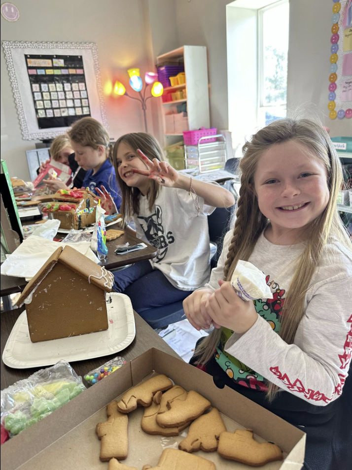 A group of children are making gingerbread houses in a classroom.