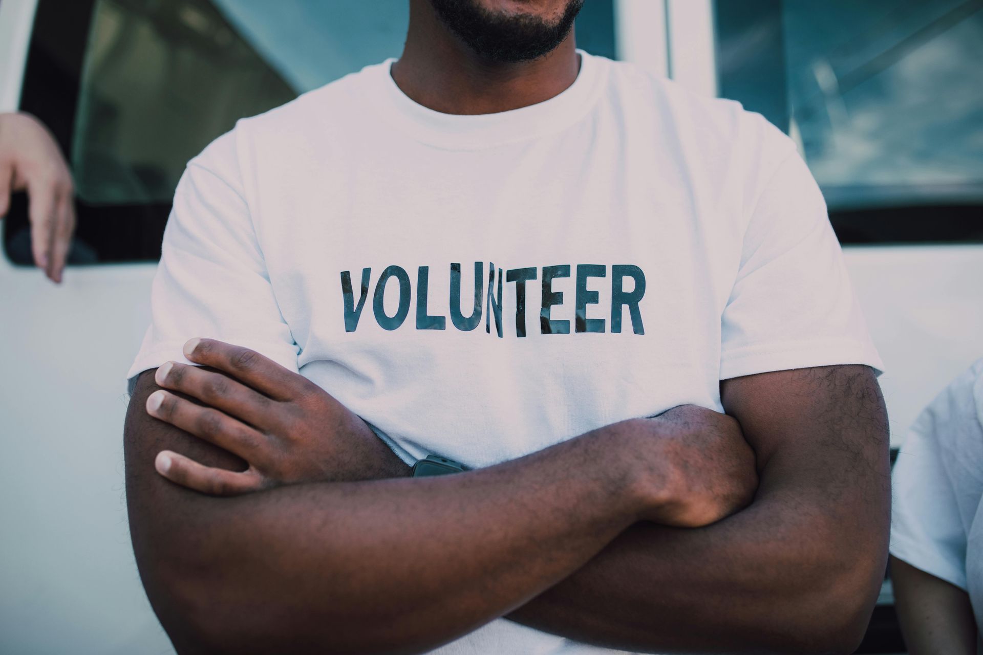 A man wearing a white volunteer t-shirt with his arms crossed.