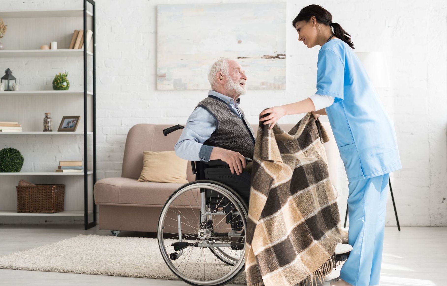 A nurse is giving an elderly man in a wheelchair a blanket.