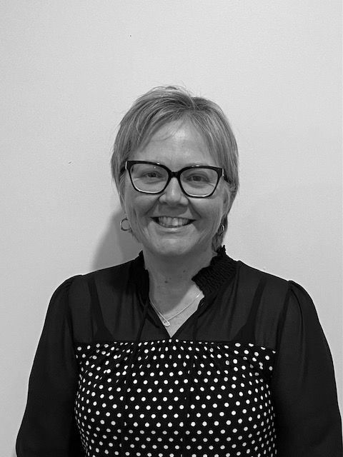 A woman wearing glasses and a polka dot dress is smiling in a black and white photo.