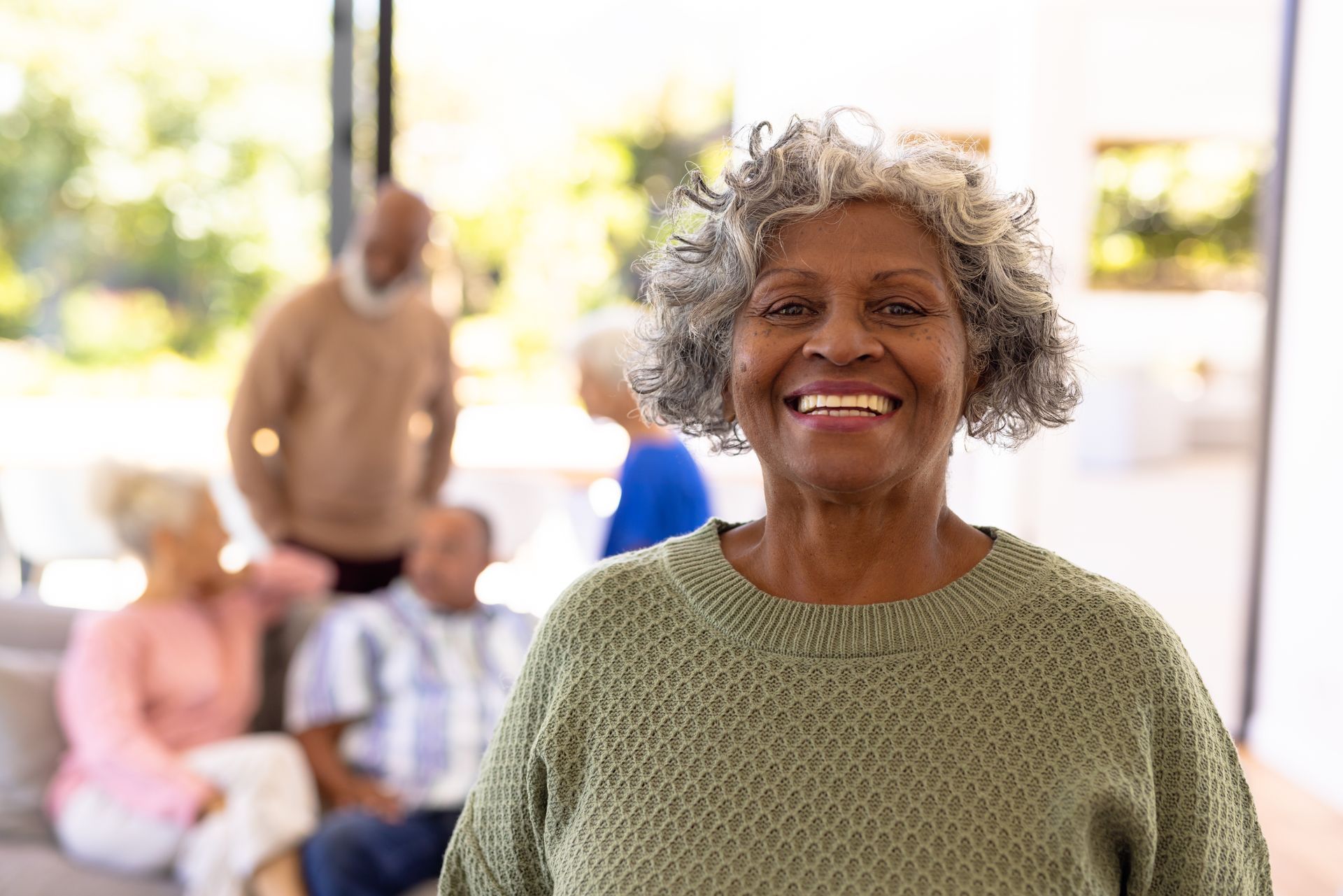 An elderly woman is smiling in front of a group of older people.