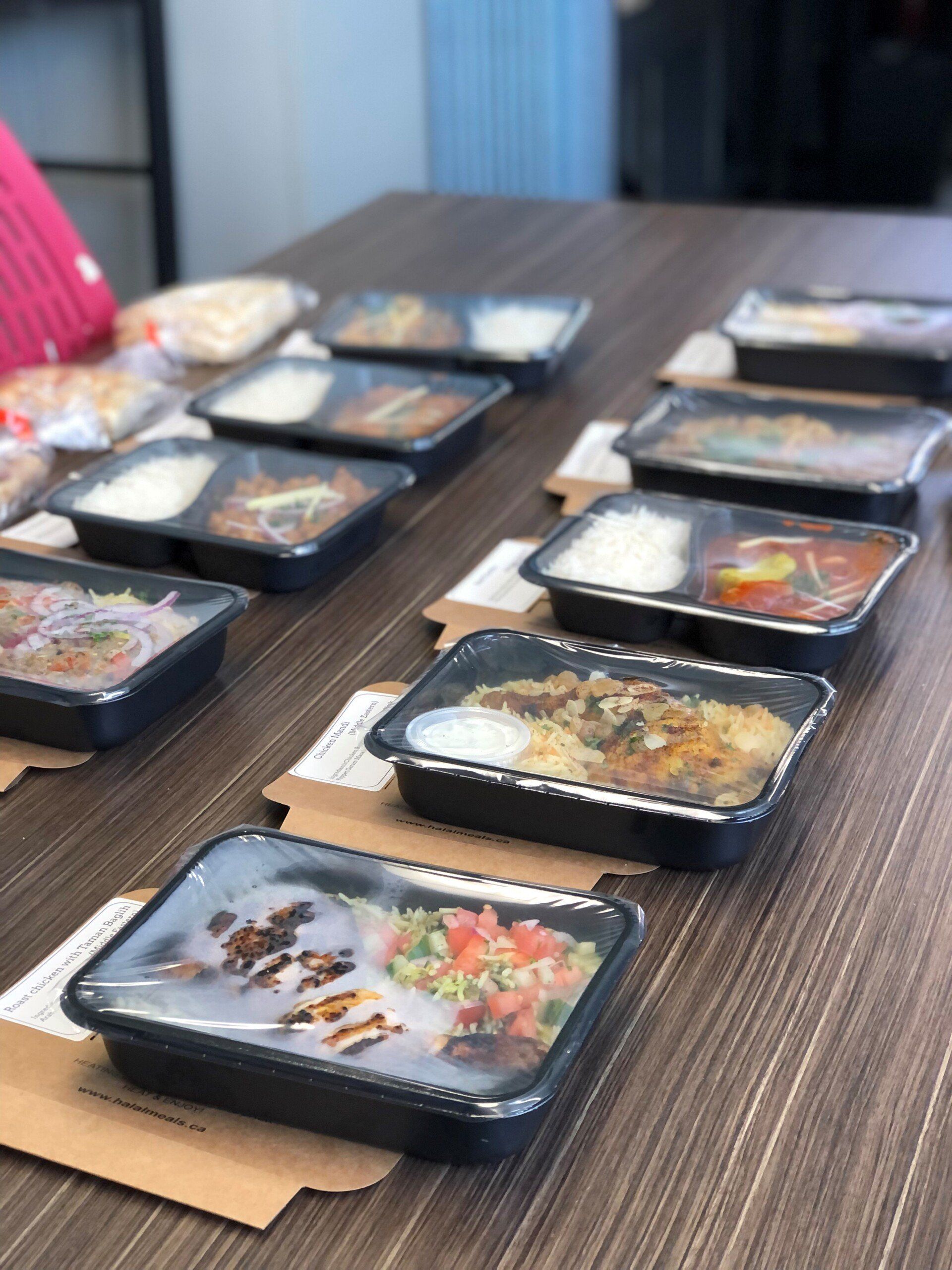 A row of plastic containers filled with food are sitting on a wooden table.