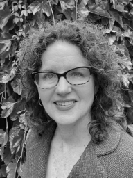 A woman wearing glasses and a jacket is smiling in a black and white photo.