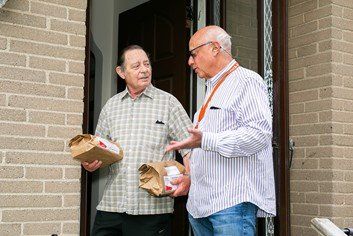 Two men are standing in front of a brick building talking to each other.