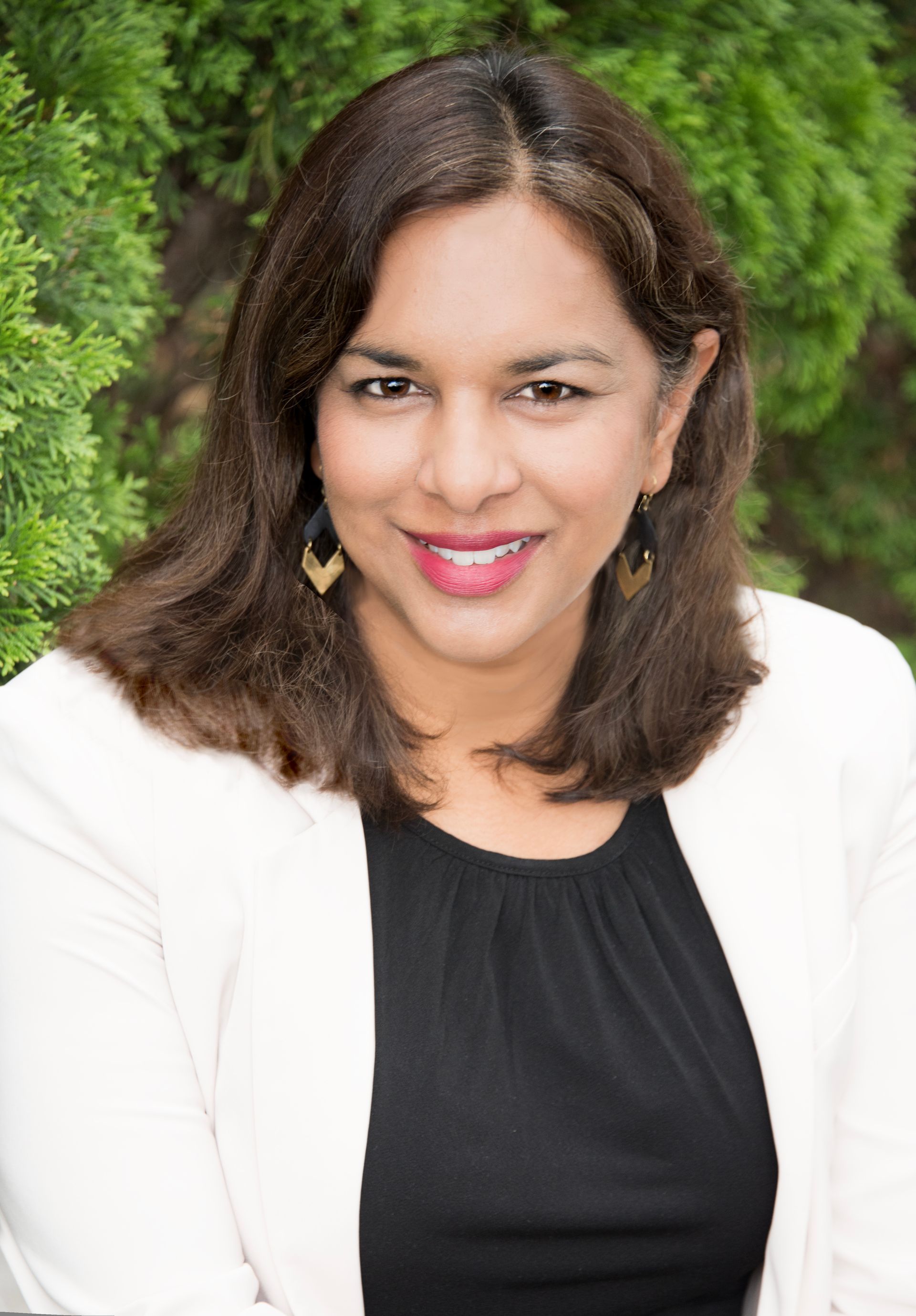 A woman wearing a black shirt and a white jacket is smiling for the camera.