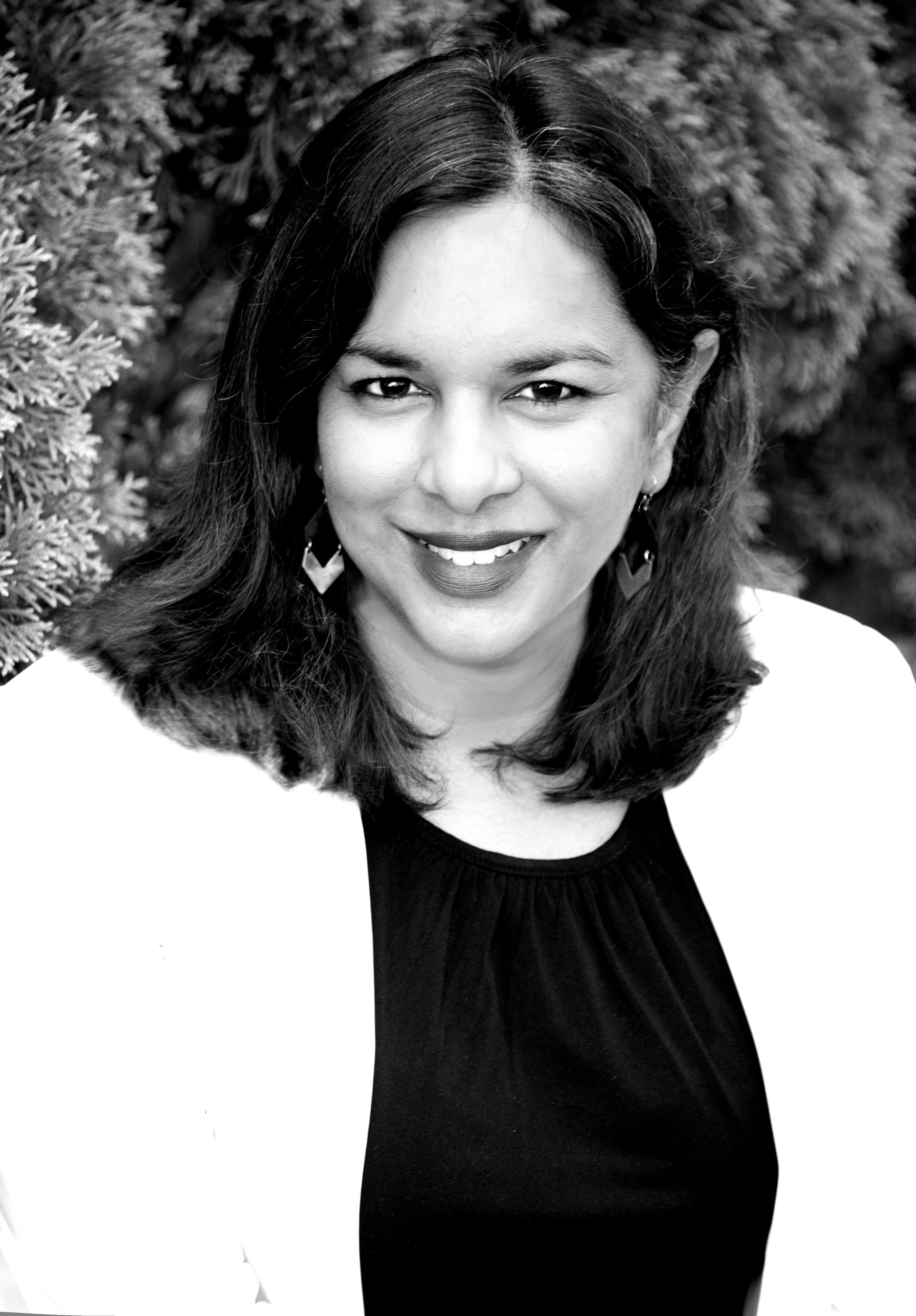A woman in a black shirt and white jacket is smiling in a black and white photo.