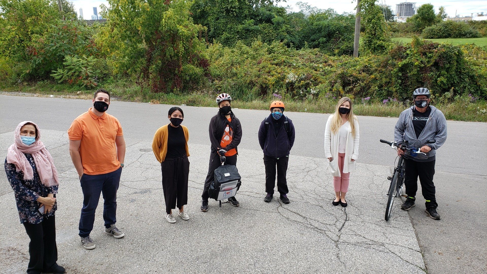 A group of people wearing masks are standing next to each other on the side of a road.