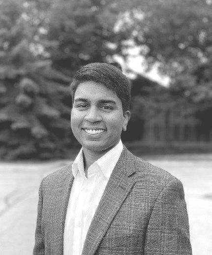 A man in a suit and white shirt is smiling in a black and white photo.