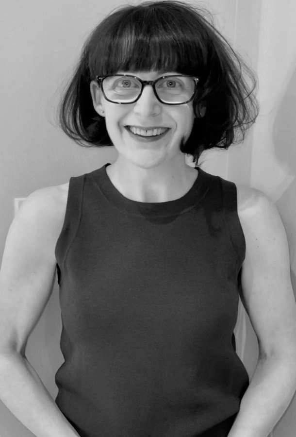 A woman wearing glasses and a black tank top is smiling in a black and white photo.
