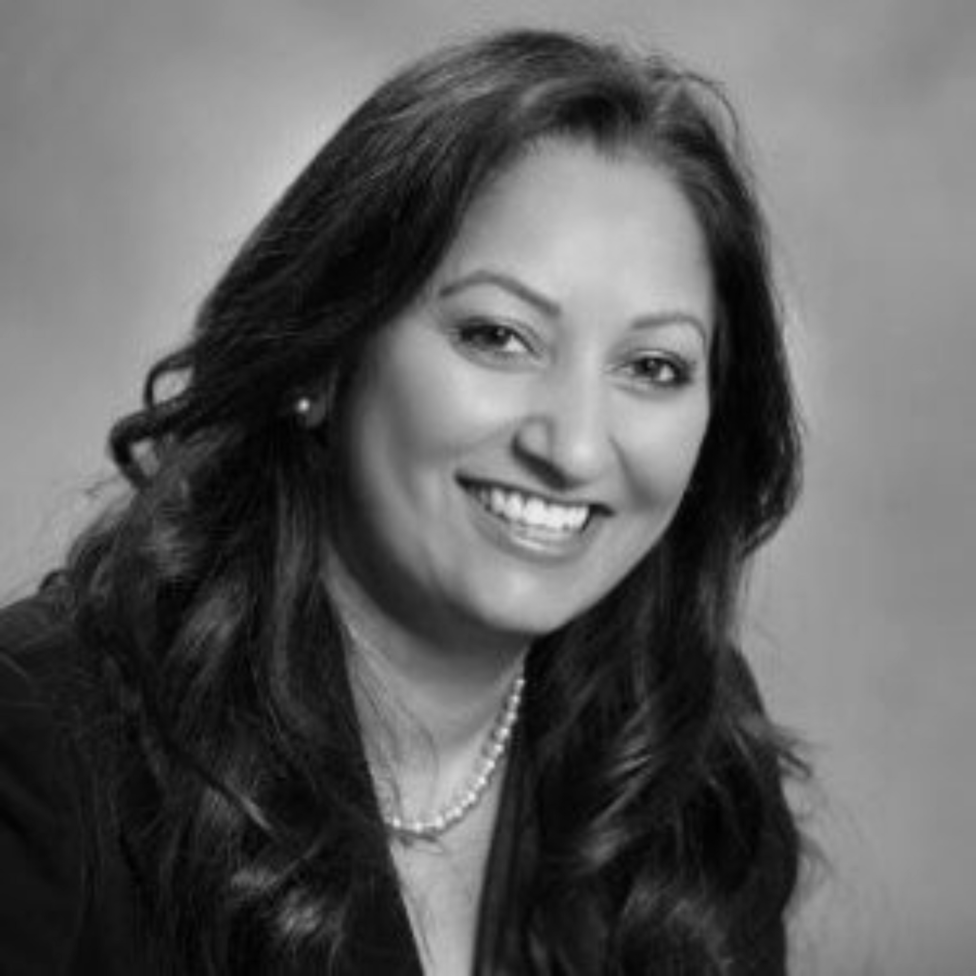 A black and white photo of a smiling woman wearing a pearl necklace.