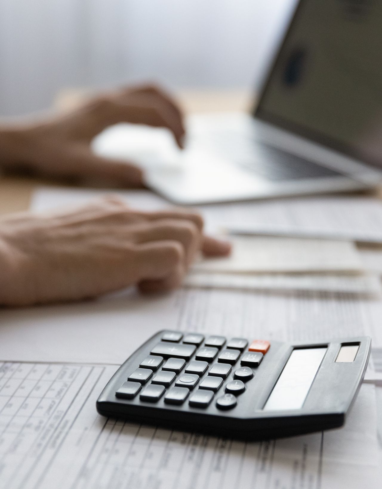 A person is typing on a laptop next to a calculator