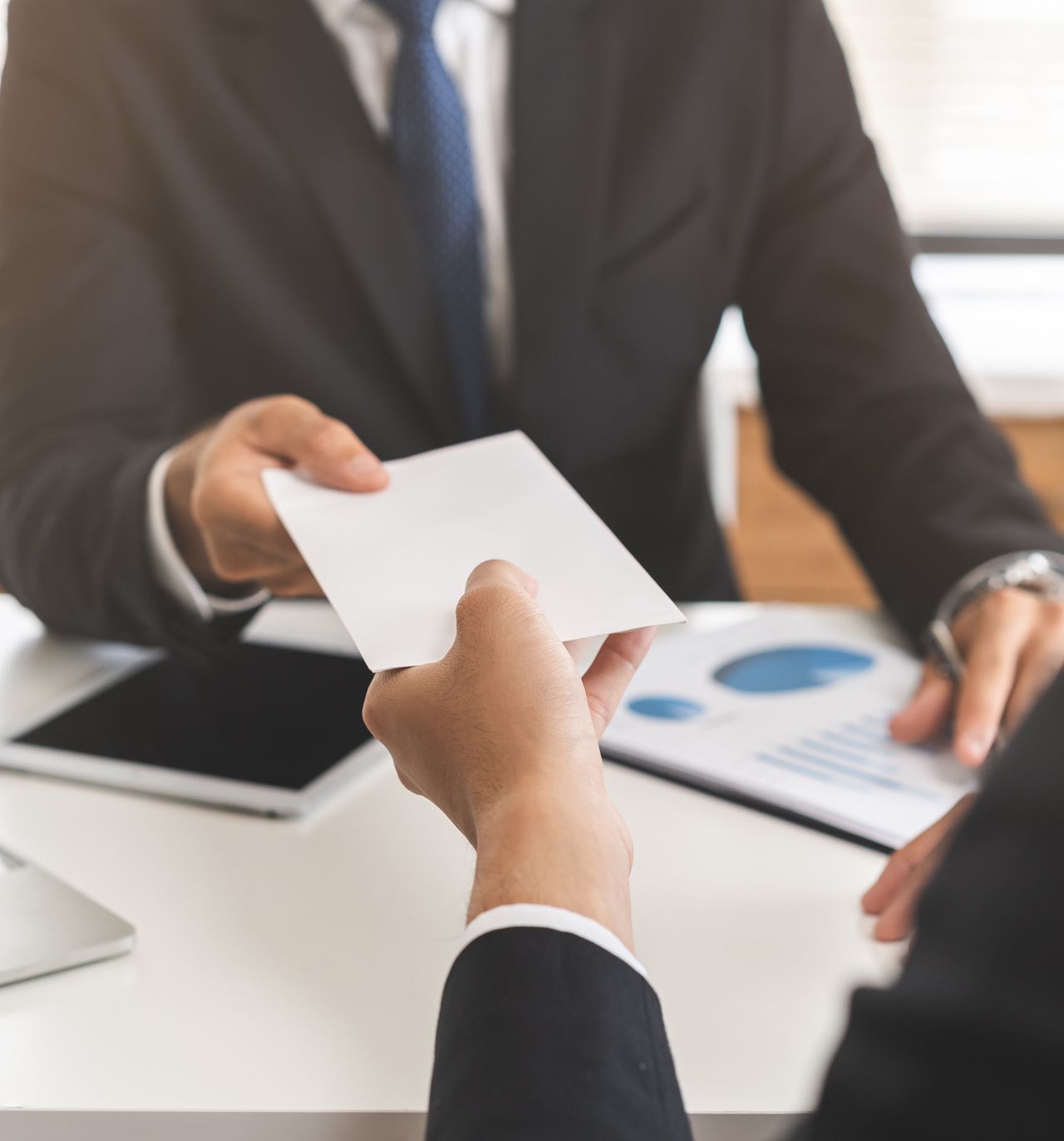 A man in a suit is handing a piece of paper to another man