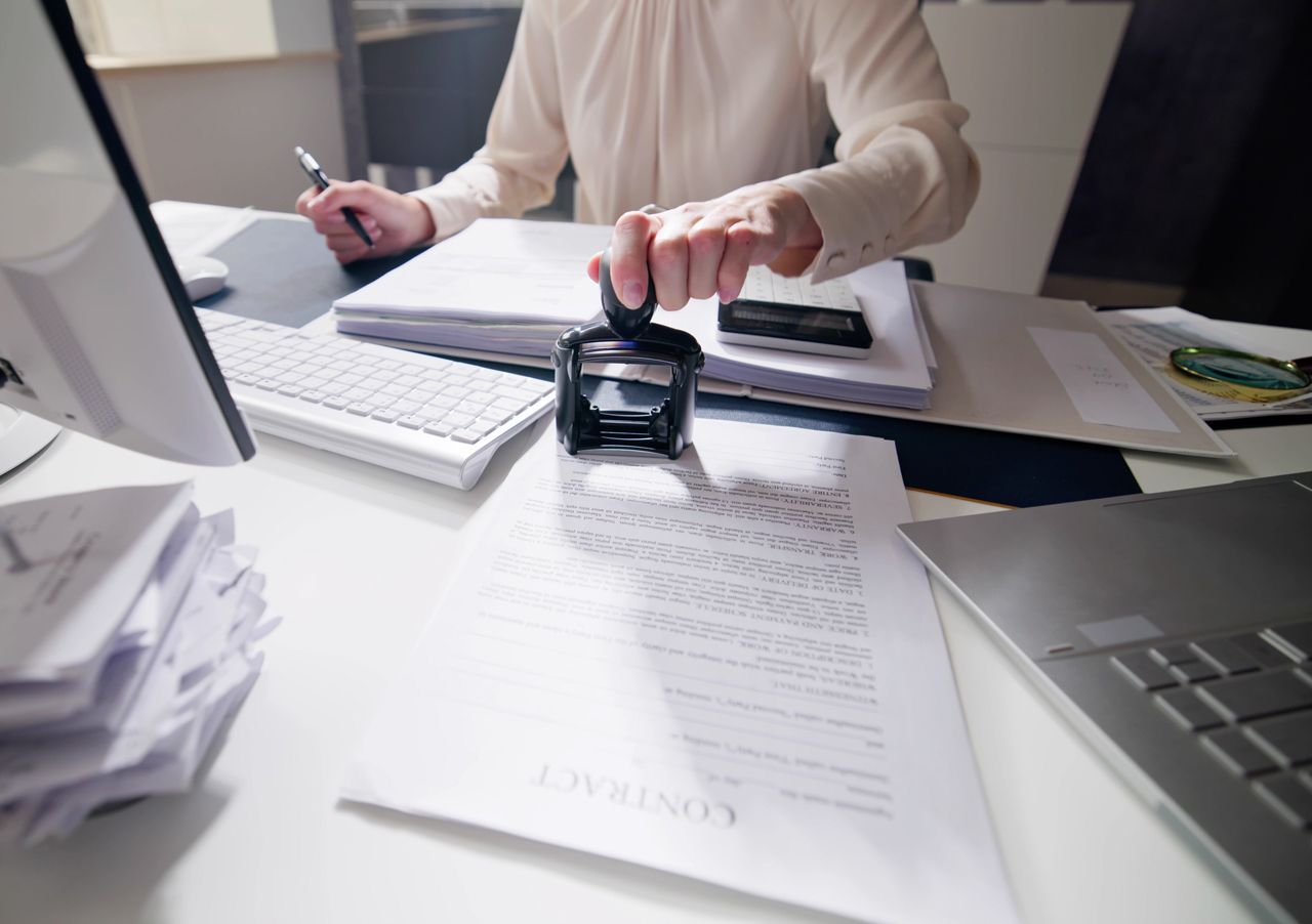 A woman is sitting at a desk using a stamp on a piece of paper.