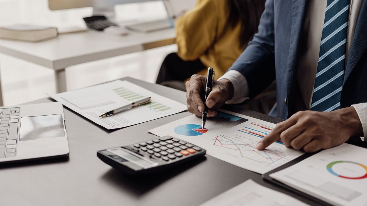 A man in a suit and tie is sitting at a desk with a calculator and a pen.