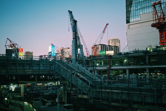 Dusk city construction site with cranes, steel framework, and a nearby glass building