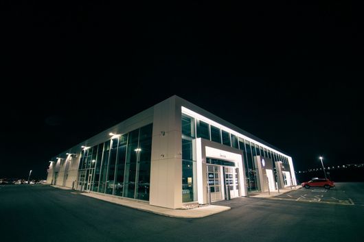 Modern glass-fronted building at night with bright interior lights and a dark parking lot
