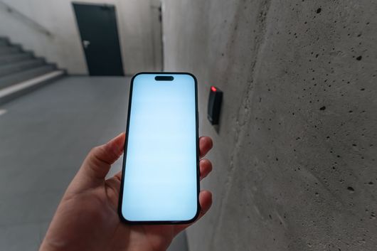 Hand holding a lit smartphone beside a wall-mounted door lock in a concrete hallway