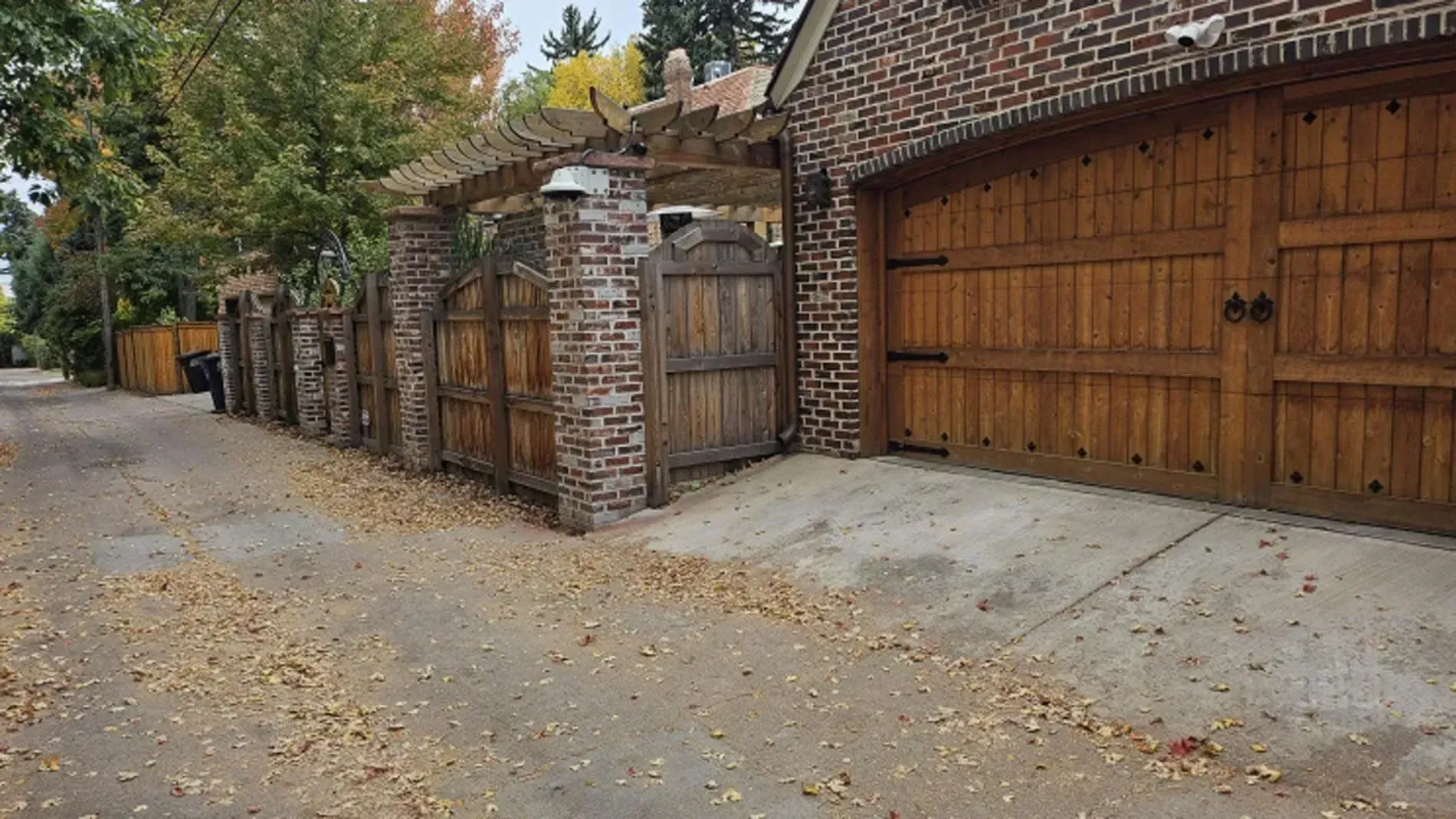 Brick-and-wood driveway gate beside a leaf-covered street in autumn