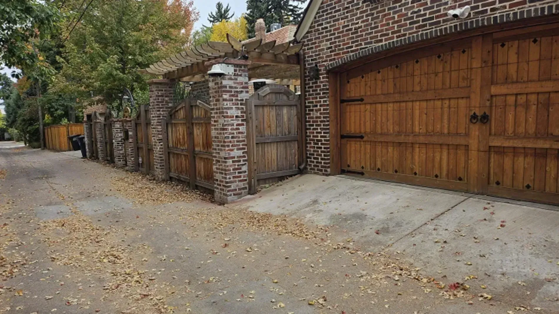 Brick wall and wooden gate along a leaf-strewn residential street in autumn