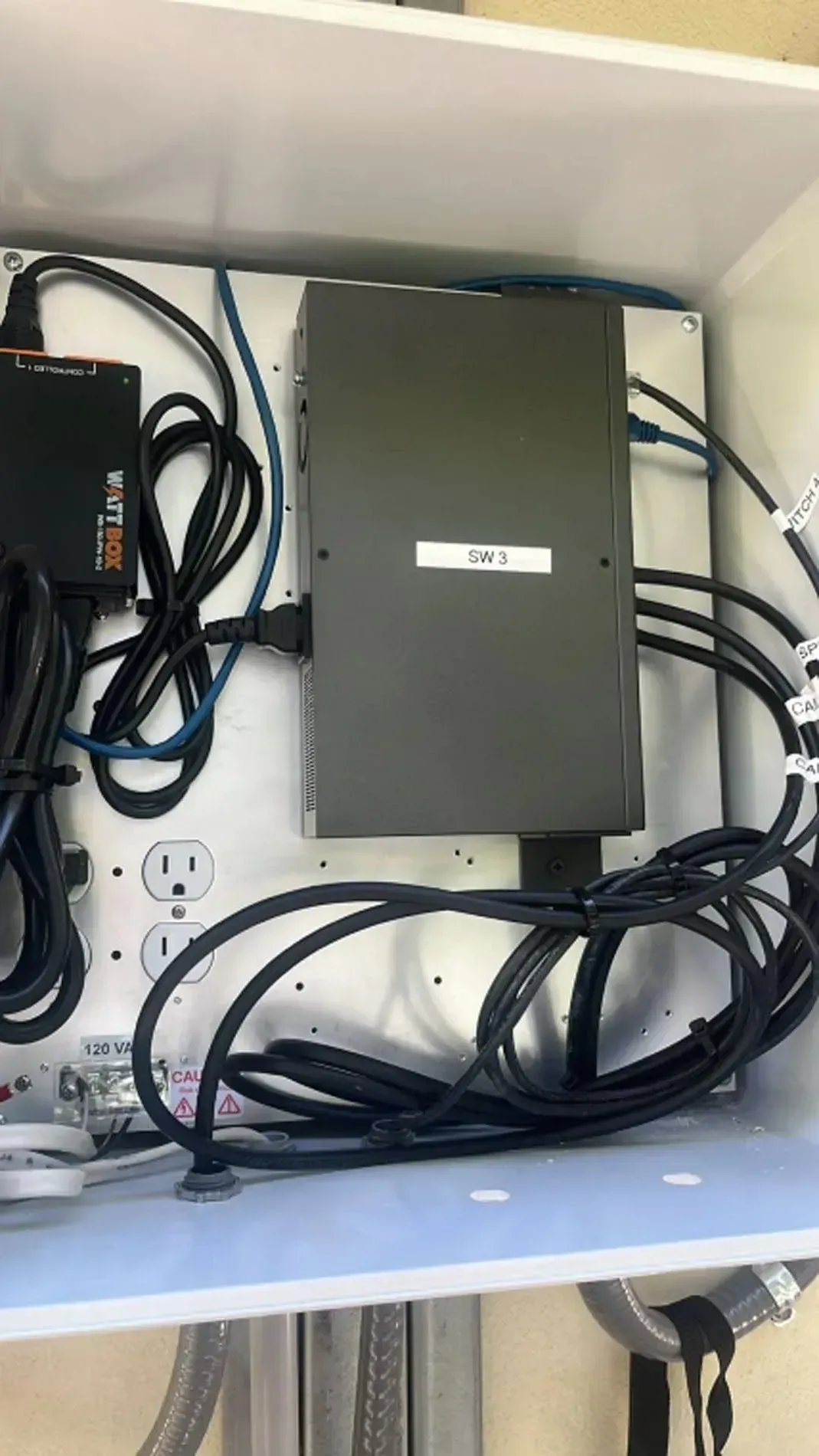 Open cabinet with a gray metal box and tangled black cables inside.