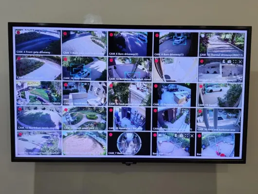 Wall-mounted TV showing a grid of CCTV surveillance camera feeds of streets and parking areas