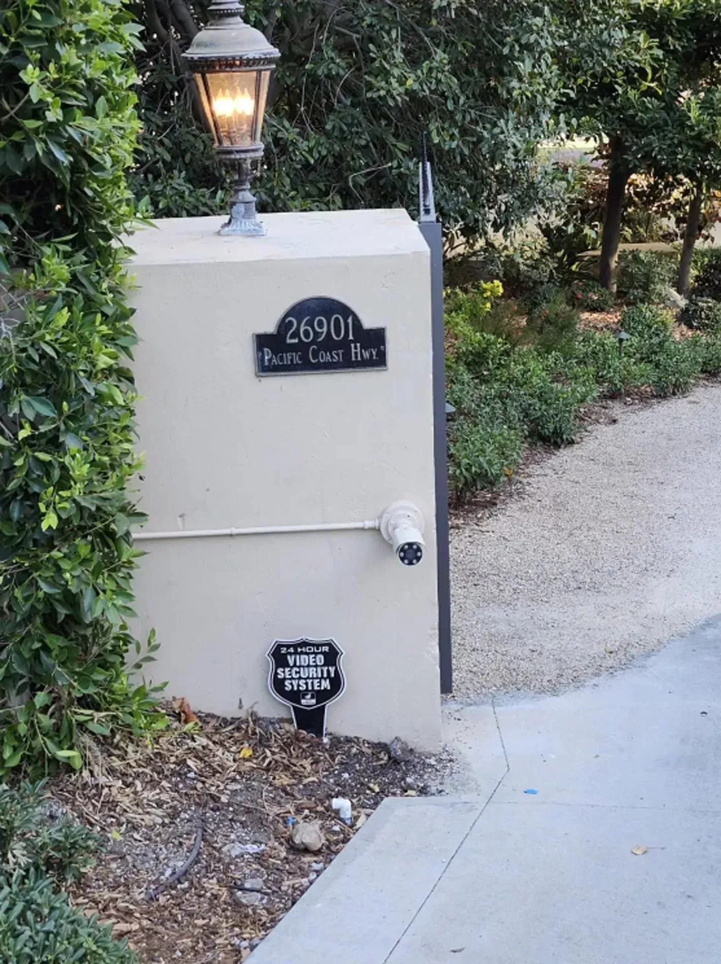 House number plaque on a stucco pillar with a lantern beside a garden path.