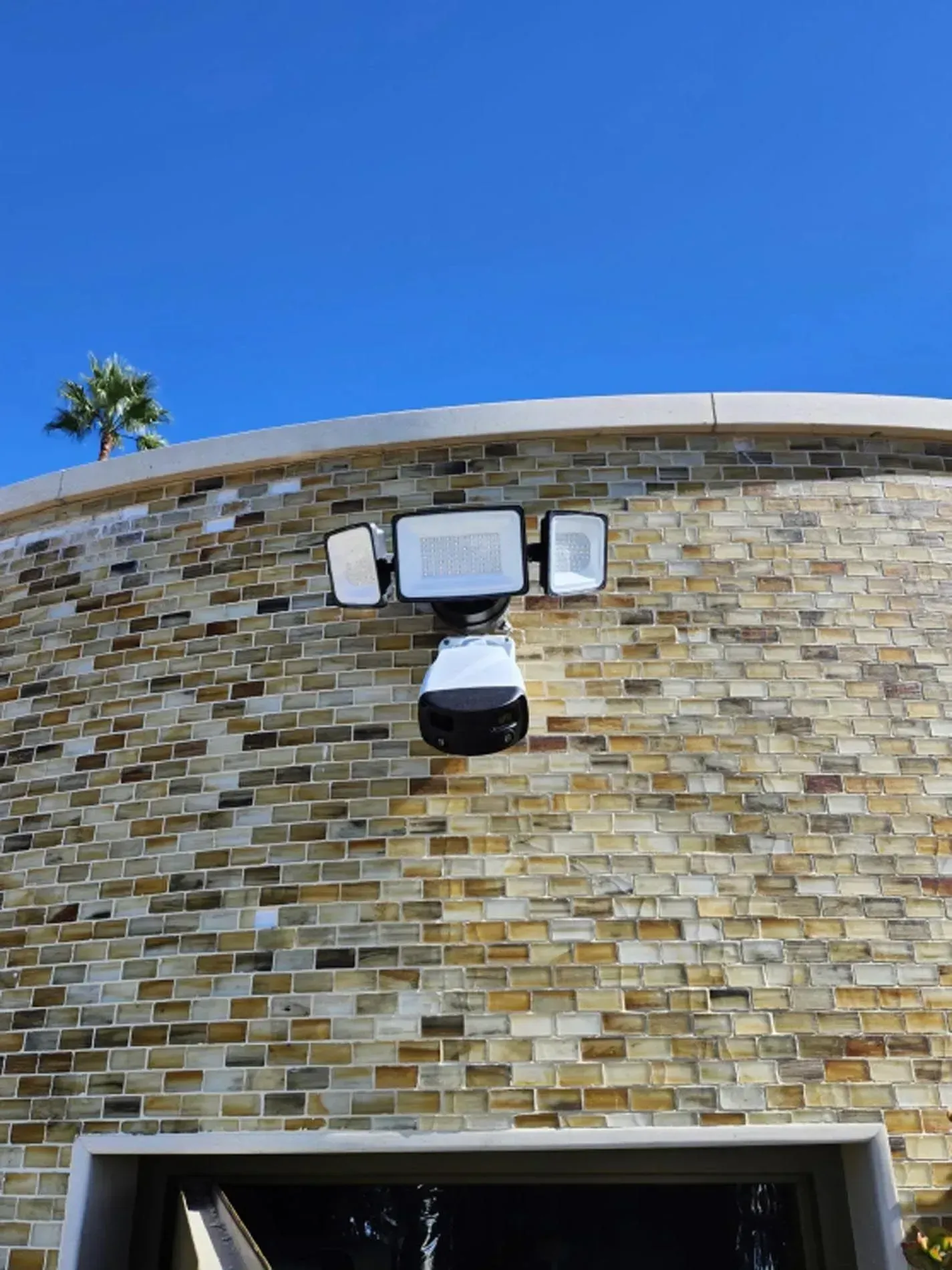 Exterior security light mounted on a stone building wall beneath a blue sky