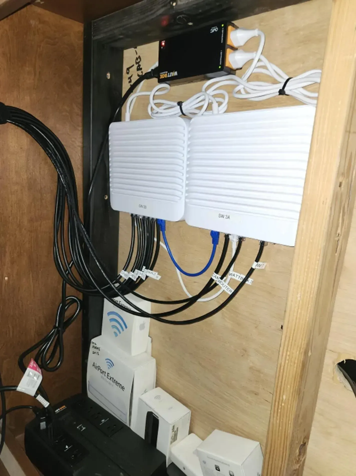 Network equipment and cables mounted inside a wooden cabinet, with two white routers or access points.