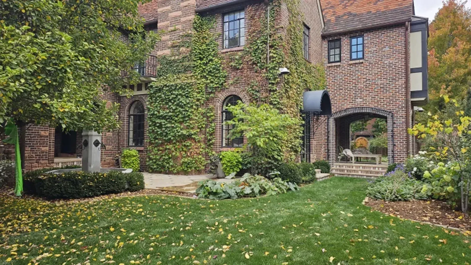 Brick house with arched doorway, large windows, and a lush green front yard in autumn.