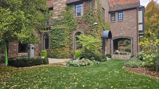 Brick townhouse with arched doorway, lush garden, and green lawn in front