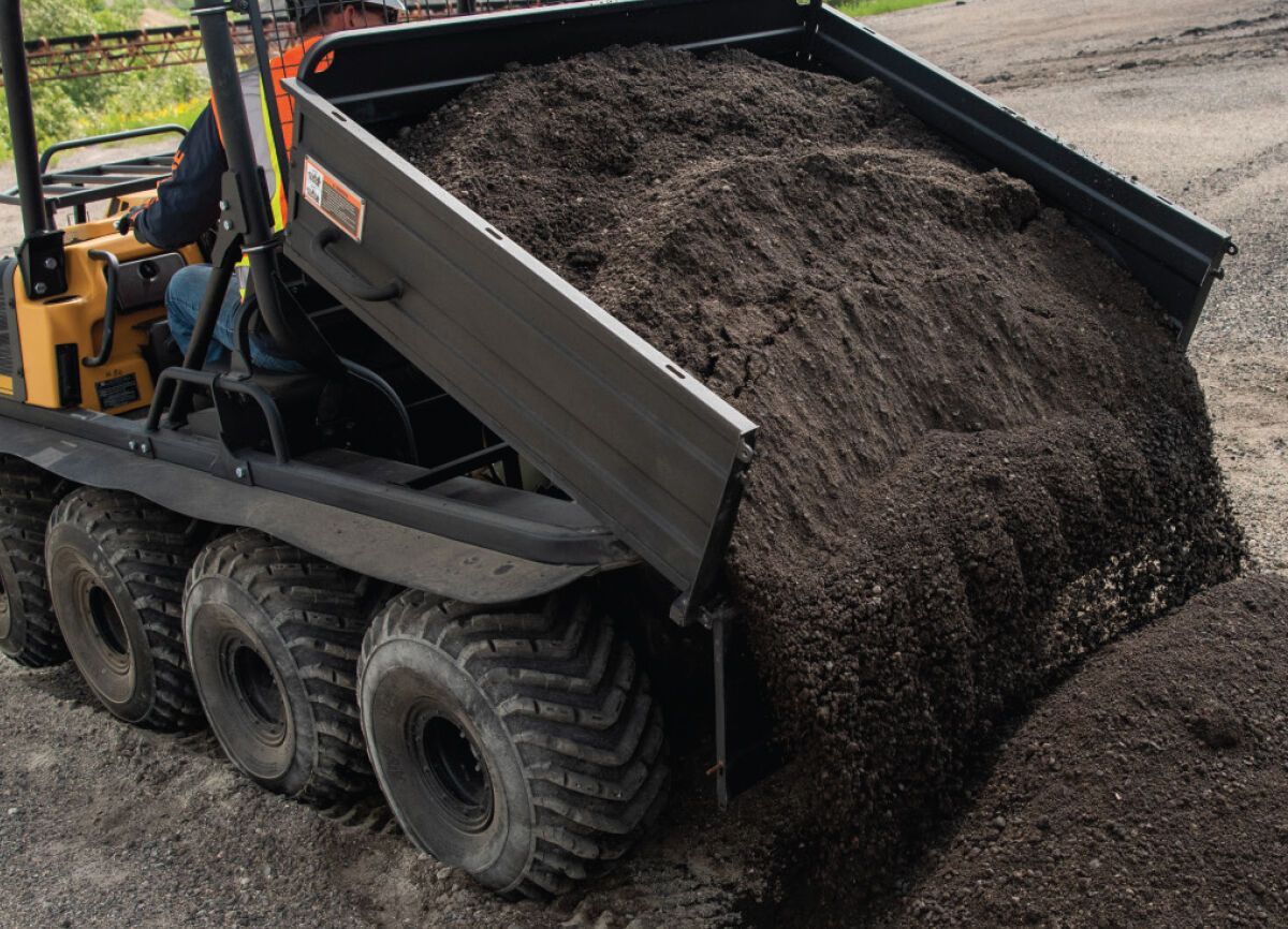 a man is driving a XTV cargo box filled with dirt