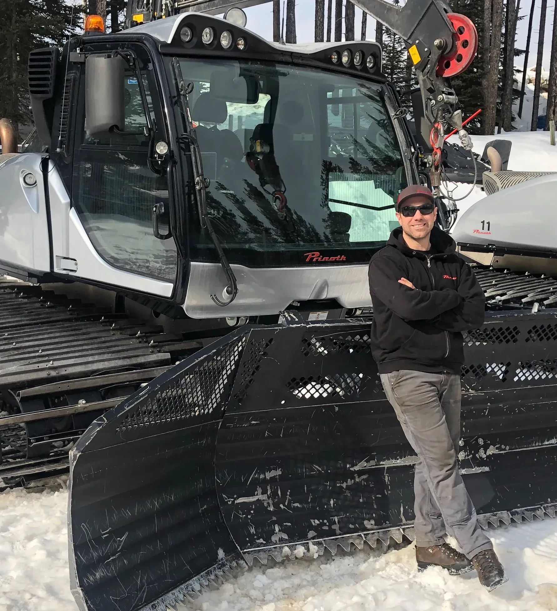 A man standing in front of a snow groomer with his arms crossed
