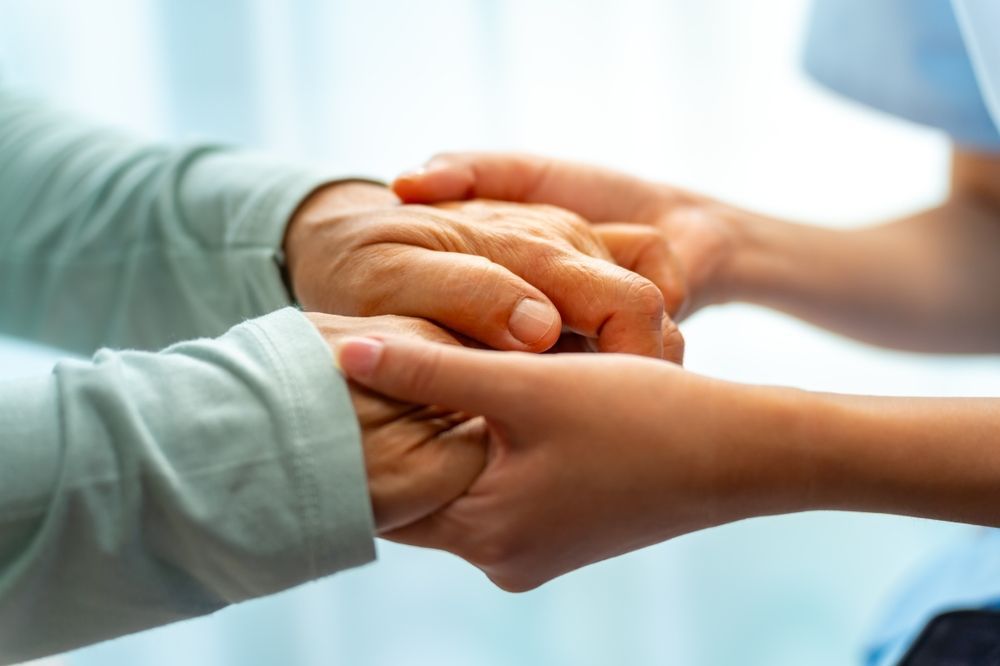 Hands of an older person held by a younger person's hands. Soft lighting.