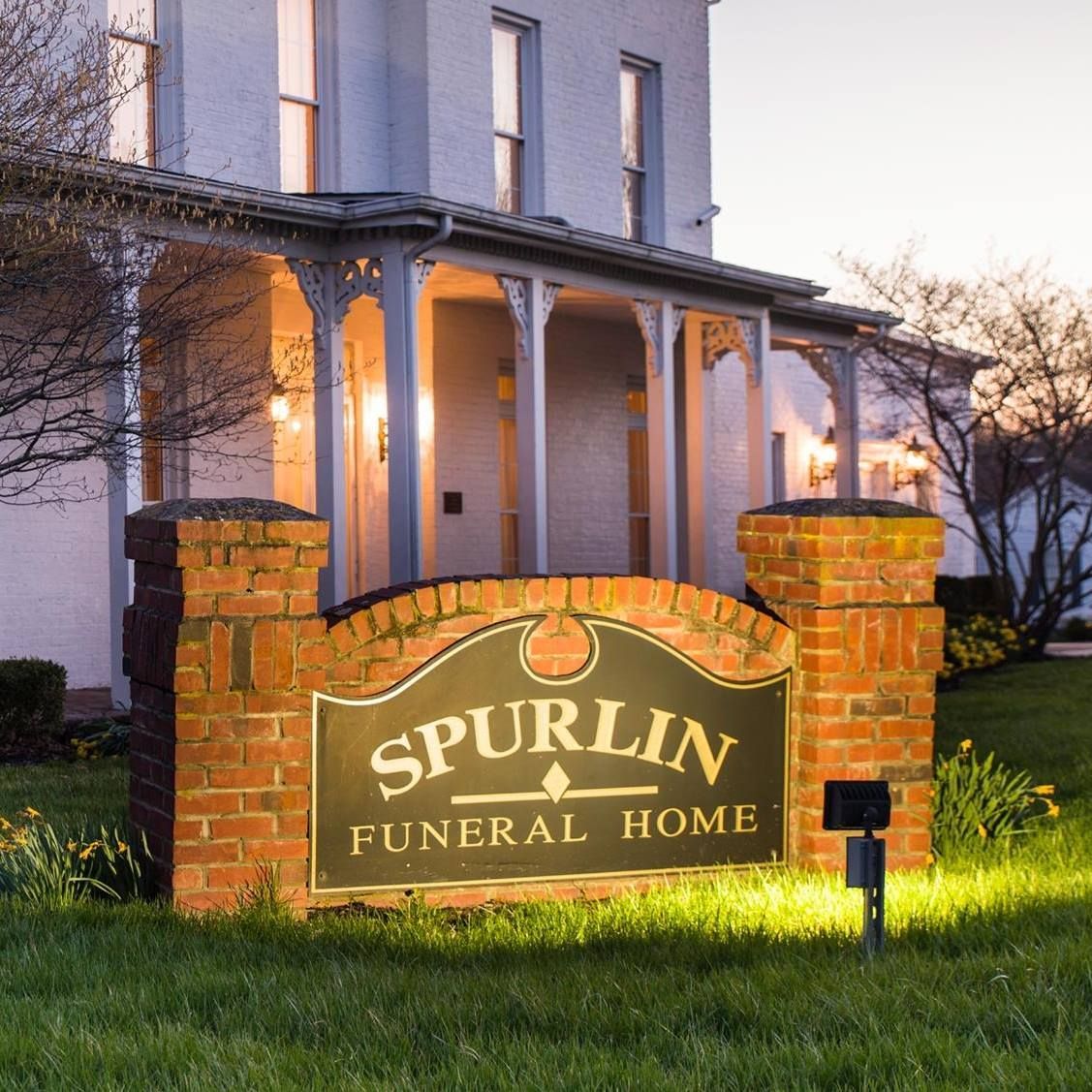 Spurlin Funeral Home sign lit at dusk in front of a white building