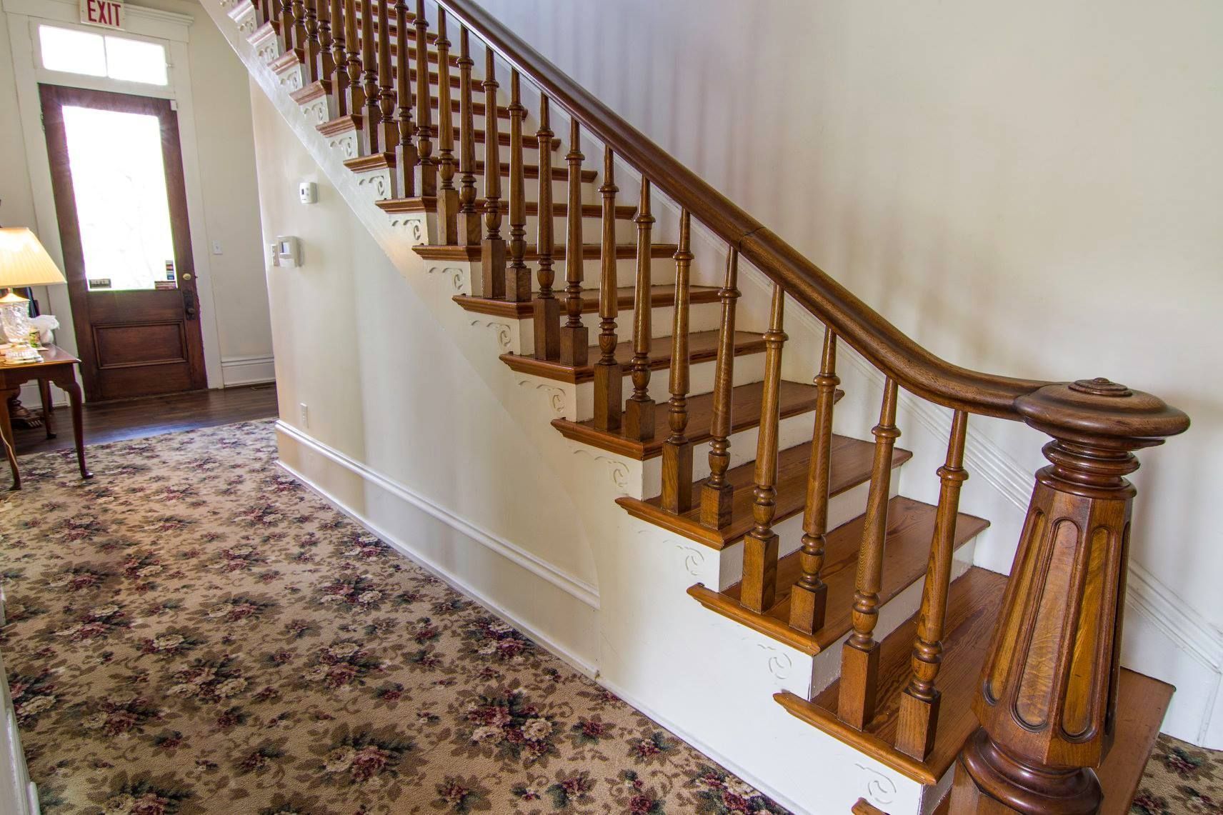 Wooden staircase with ornate banister along a hallway with floral carpet and white walls