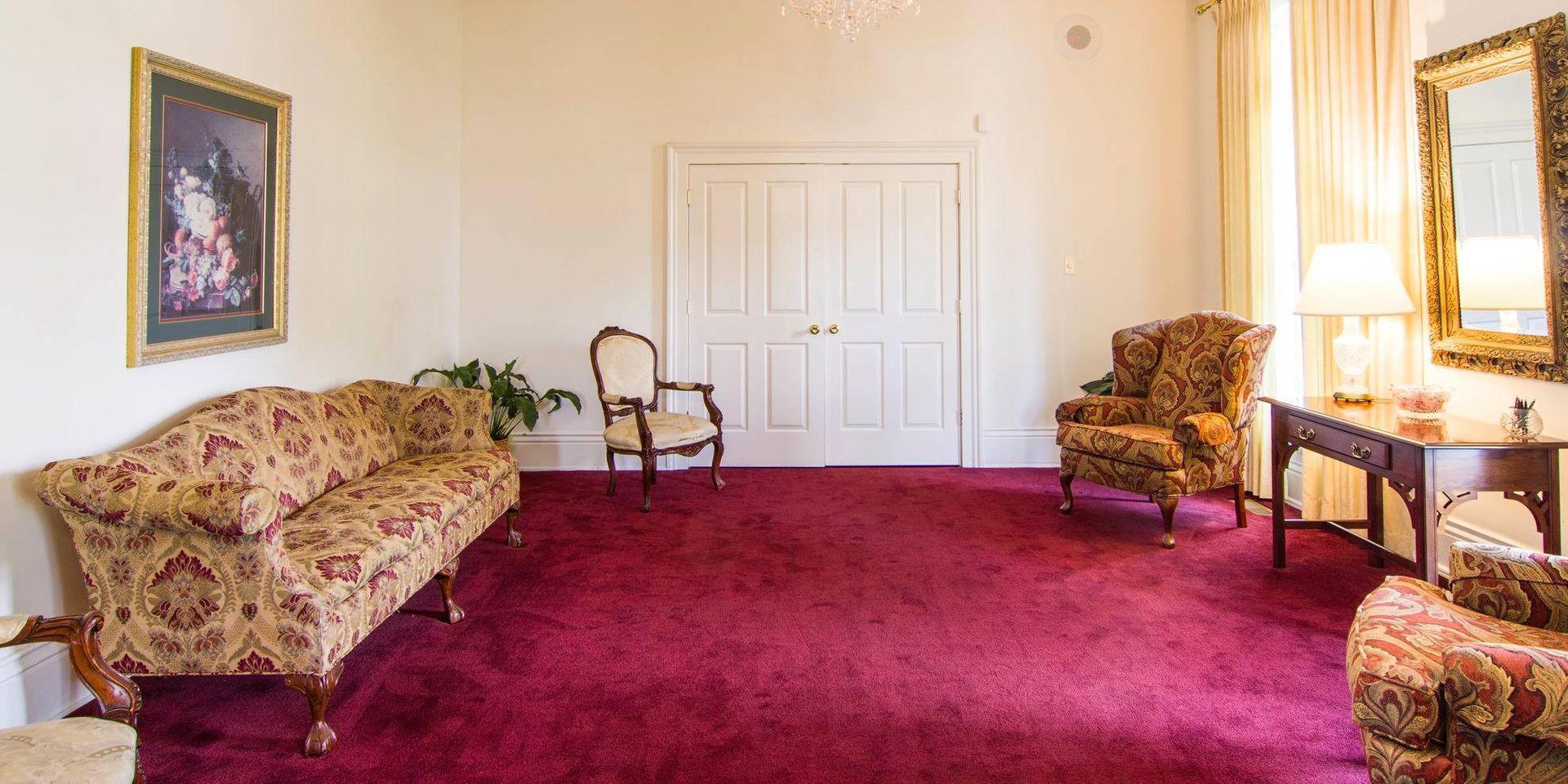 Elegant living room with burgundy carpet, floral sofa and armchairs, white doors, and framed wall art