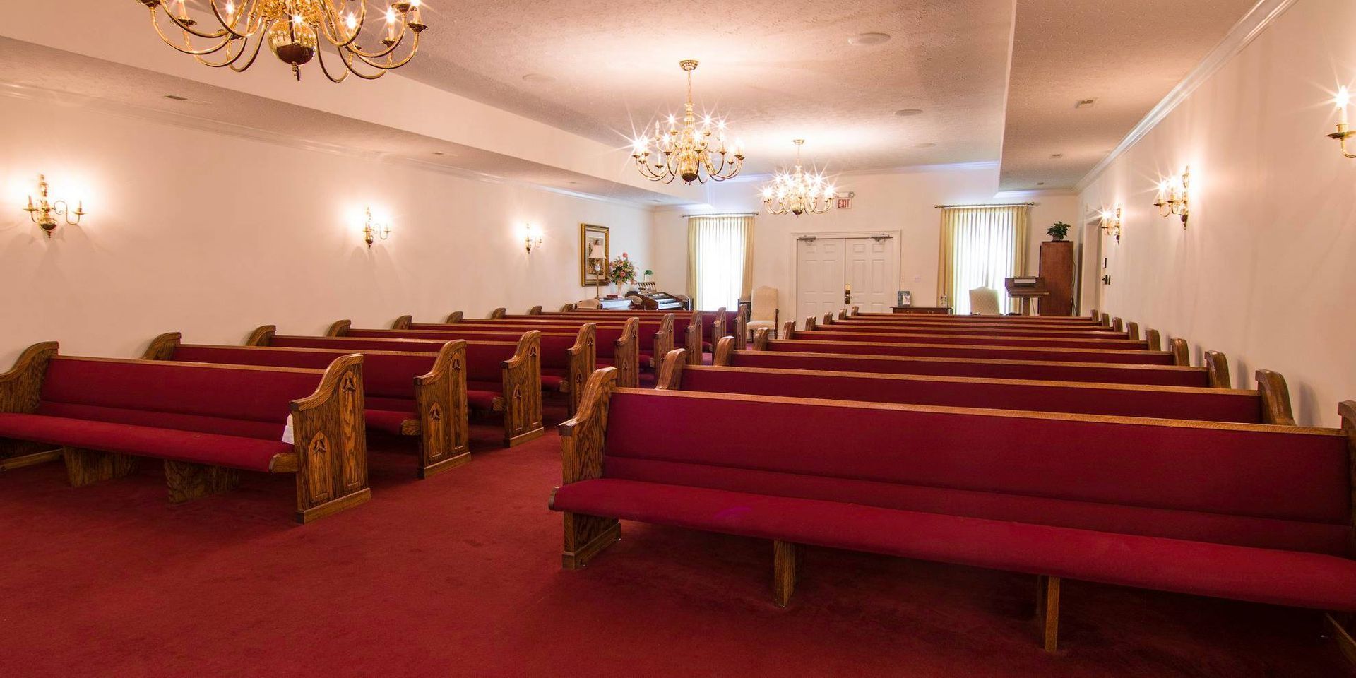 Empty church sanctuary with red pews, chandeliers, and white walls